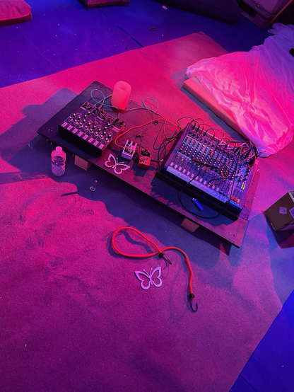 picture from an experimental live performance with a synth, fx pedals, a mixtable and some metal butterflies, the whole bathed in pink light