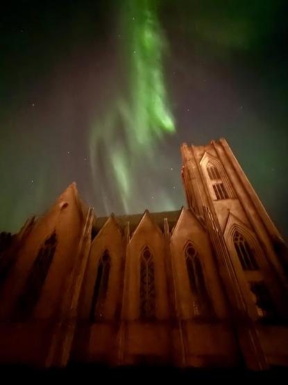 Green northern lights dance above the side view of Landakotskirkja 