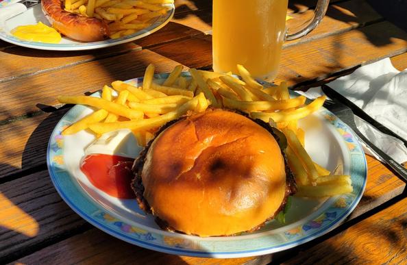 Teller mit Veggieburger und Pommes auf Holztisch, daneben ein trübes Bier