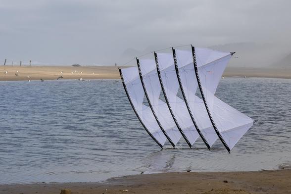 A white 5-stack of quad kites touching the water