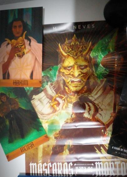 Pôster aberto. Uma variação da capa, mas com mesmo conteúdo. Ao lado dele, cartão com o personagem Hakim, um homem moreno de cabelos longos tirando uma máscara dourada do rosto, e de Moira, uma mulher vestida de pele de animal segurando uma espada longa. Ainda, à direita, o marcas páginas.