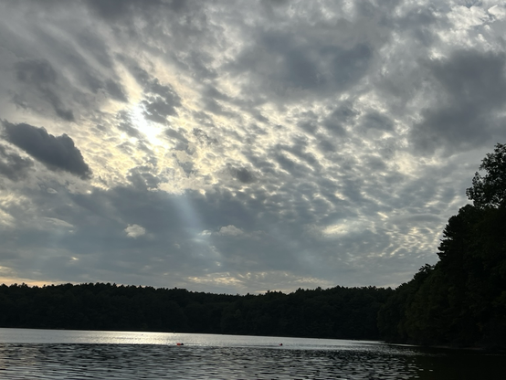 A few bright rays of sun coming out of a modeled sky, beaming down onto Waldin Pond a dark ring of trees on the far shore is visible
