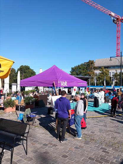 Stand von Volt mit 2 Besuchern im Gespräch mit uns.
Im Hintergrund das Treiben auf dem Neuen Markt.