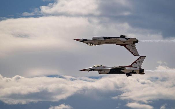 Two U.S. Air Force Thunderbird F-16 jets fly in mirror formation at the Great Colorado Air Show in Loveland, Colorado, with one aircraft inverted above the other against a cloudy sky.