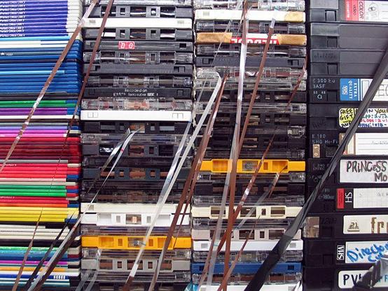 Patron economy: photograph of a stack of "old" media: floppy disks, cassette tapes, VHS tapes. Image attribution: Flickr user fernando