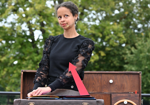 Sia hat eine Seite im Pop-Up Buch umgeschlagen. Aus dem Buch ragt ein recht großer roter Pfeil, der auf sie zeigt.