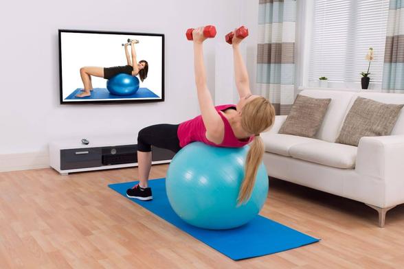 Woman doing a home workout on a mat with stability ball and dumbbells — affordable home fitness setup.