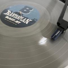 Nahaufnahme einer grauen Vinyl-Schallplatte auf einem Plattenteller mit einer über der Platte positionierten Abtastnadel. Auf dem Etikett steht der Text "Rantanplan" und "Blast-NY".