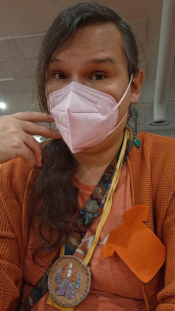 Selfie. Wearing my orange shirt and cardigan along with my traditional necklaces. Wearing a mask because public spaces.