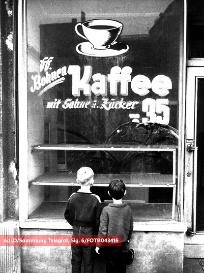 Schwarz-Weiß-Foto, zwei Jungen stehen mit dem Rücken zur Kamera vor einem leeren Schaufenster mit Aufschrift "Bohnen-Kaffee mit Sahne u. Zucker .-35