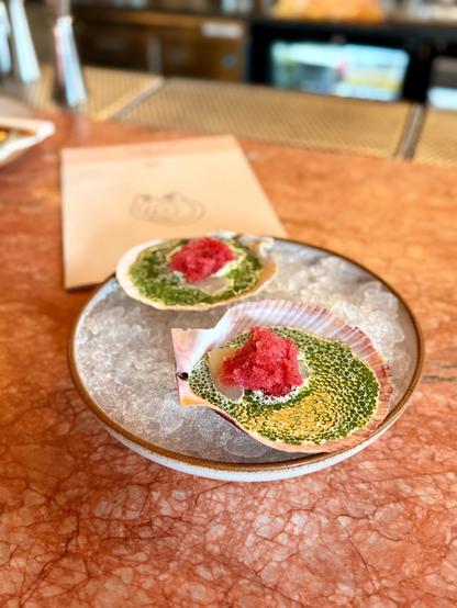 The scallops at Skál are the signature dish. Raw scallops, with a red currant granita, horseradish cream & dill oil. The plate has two scallops. 
