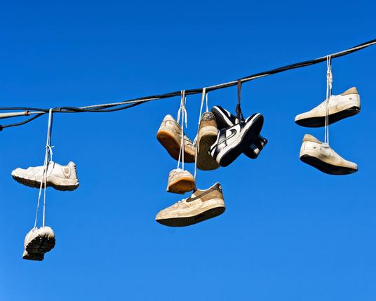 A powerline consisting of two black wires wound around a spiral cable  has about five pairs of shoes wrapped around it