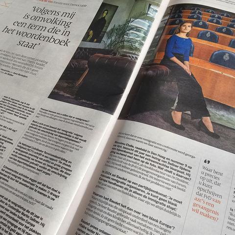 Een opengeslagen krant met een interview en een grote kleurenfoto van FvD lijsttrekker de Vos in een blauwe top en zwarte rok, zittend op de rand van een bank met achter haar een zaal met blauwe stoelen. Op de linkerpagina staat in grote letters het citaat: "Volgens mij is omvolking een term die in het woordenboek staat". Rechts onderaan staat een uitvergroot citaat: "Waar bent u precies op uit, dat u kunt opschrijven dat FvD van azc’s een gevangenis wil maken?". De rest van de pagina’s zijn gevuld met tekst in kolommen en kleinere vragen en antwoorden.