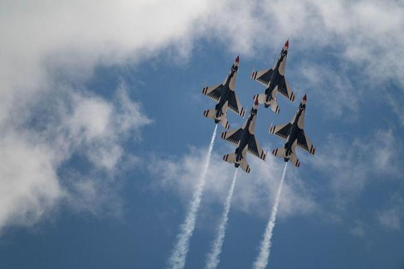 Four USAF Thunderbirds jets in tight diamond formation climbing vertically with white smoke trails, framed against blue sky and light clouds at the Great Colorado Air Show.