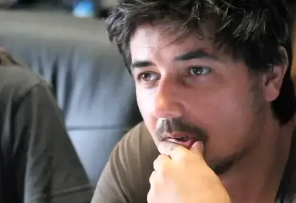 Amon Tobin, musicien électronique, compositeur et producteur brésilien : sa main droite est posée sur son menton ou sa bouche, un geste qui suggère réflexion ou introspection.