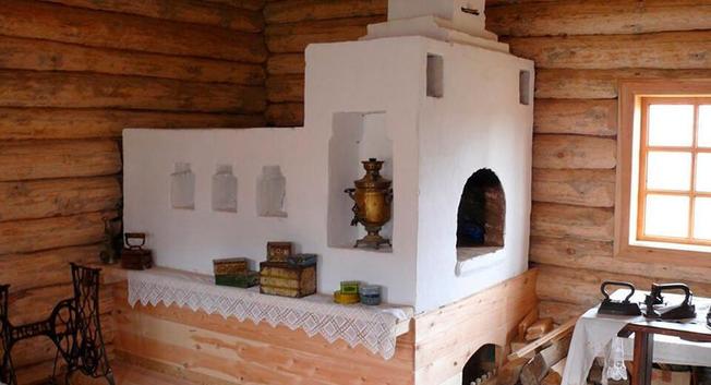Vintage Russian-style whitewashed brick oven in a log cabin with a Samovar on the side.
