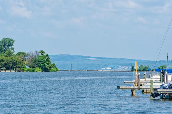 A body of water is visible protected by a jetty in the distance with just a little bit of dock extending in from the right and a shore with trees on the left.  In the far distance is a line of hills past the lake in the haze.