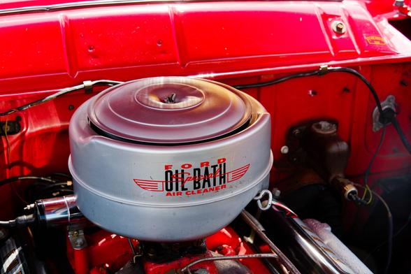 A short and wide white cylinder reads FORD OIL BATH AIR CLEANER inside an engine bay which is mostly red with some black and chrome parts.
