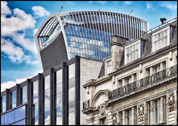 Architekturfotografie mit Blick auf zwei Gebäude in der Londoner City.
Linksstehend ein modernes, ganz mit Glas aufwendig verspiegeltes Hochhaus, in dem sich der blaue Himmel mit Wolken spiegelt.
Direkt daneben steht ein altes, mit Bogen, kleinen Balkonen, Figuren und alten Fassadenelementen verziertes Haus, hochherrschaftlich und mit Spuren der Jahrhunderte.