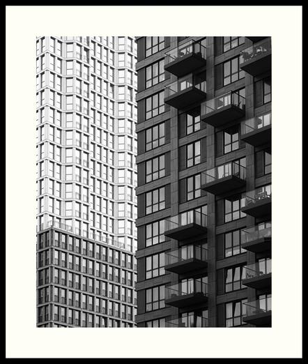 b&w - A tightly framed photo of the De Kroon and Wijnhaven residential towers in downtown The Hague. The building on the left, De Kroon, features a repetition and multitude of floor-to-ceiling windows and its design is inspired by the Chicago skyscrapers from the early 1900s. The building on the right is interspersed with what seems like randomly placed balconies.