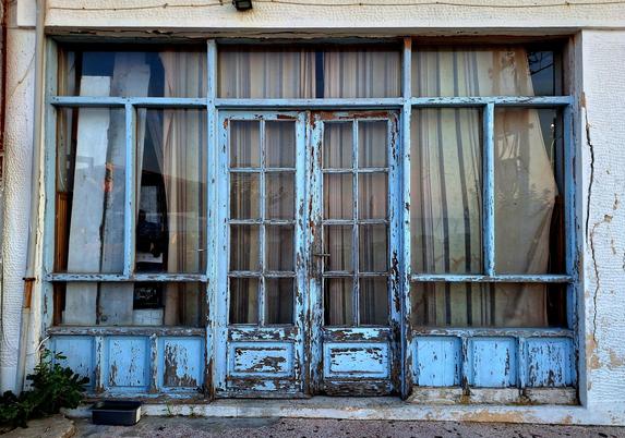 Picture of a glass storefront with a door at the center. The frames are painted light blue, with the paint peeling off.