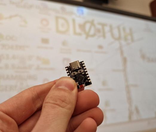 Human hand holding a ESP32-C3 SuperMini in front of desktop background saying DL0TUH