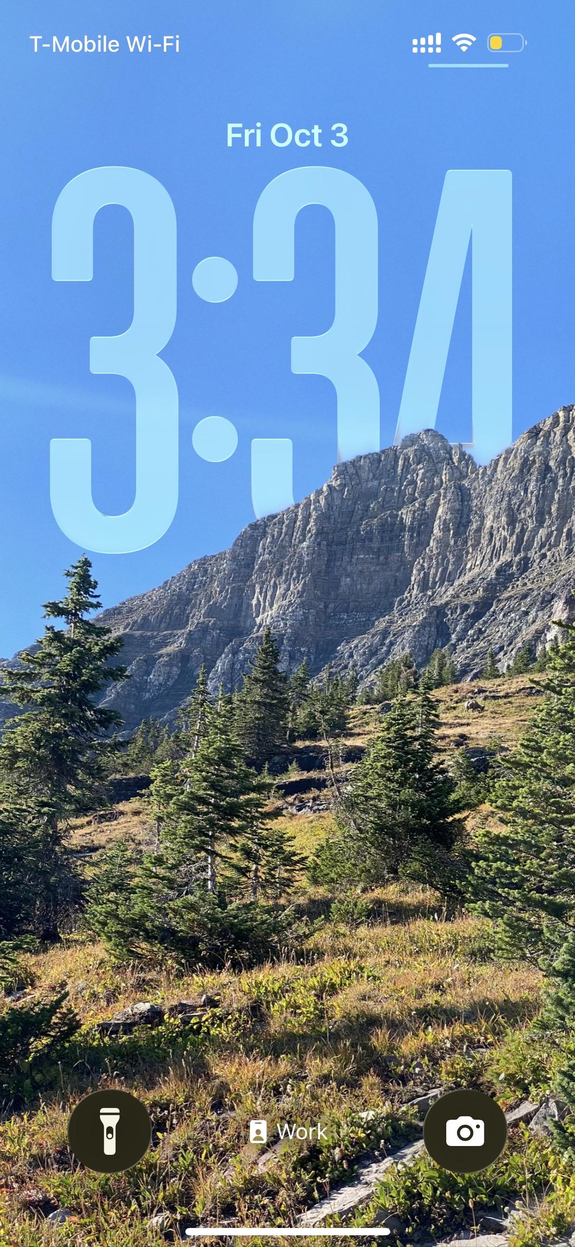 A scenic view of a mountainous landscape with coniferous trees in the foreground and a clear blue sky. The time displayed is 3:34 PM on Friday, October 3. Various mobile interface elements are visible at the top and bottom of the screen. 