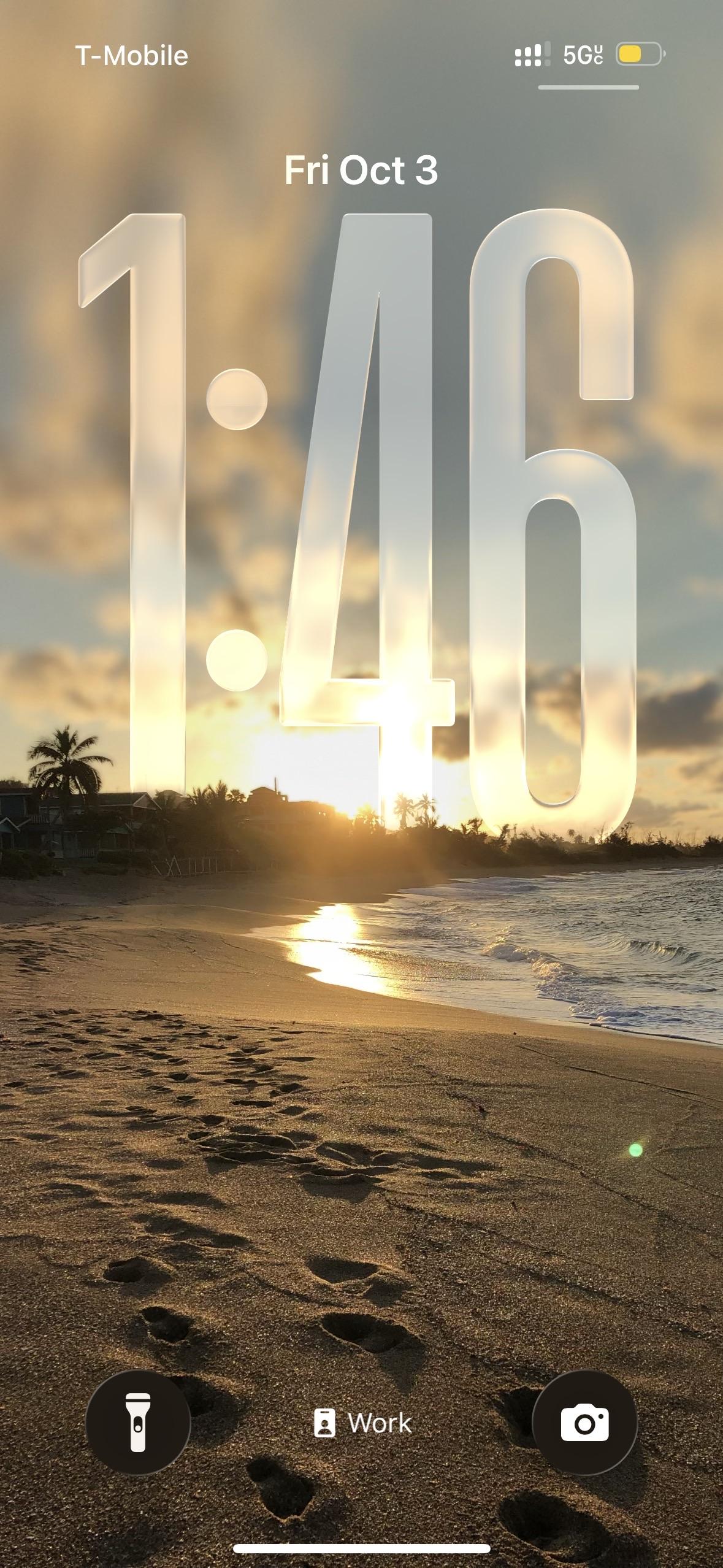 A beach scene at sunset, showcasing golden sand with footprints leading toward the water, and a bright sun setting on the horizon. The time reads 1:46, and the date is displayed as October 3.