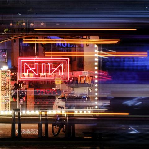 a view of the Nine Inch Nails neon sign hanging in Sonic Boom on Spadina in Toronto, from across the street where a passing firetruck leaves light streaks behind during a 1/4s exposure. 