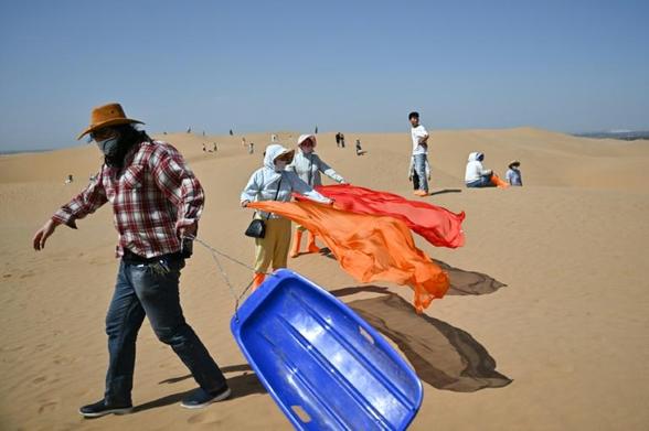 Des touristes dans le désert de Kubuqi, près d'Ordos, dans le nord de la Chine, le 11 août 2025 (AFP/Archives - Pedro PARDO)

Ces projets agrovoltaïques  doivent aussi composer avec l'essor du tourisme, qui a explosé dans le désert de Kubuqi, stimulé par les vidéos d'expéditions en quads ou de balades en dromadaires.