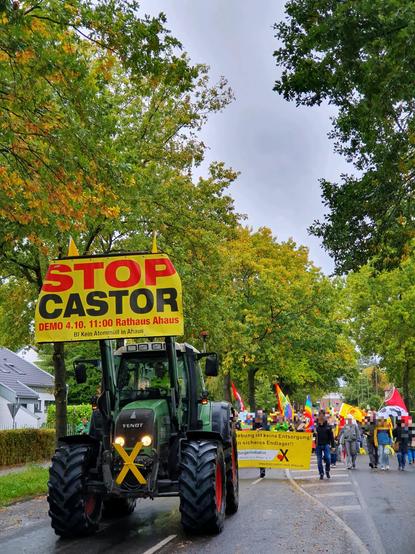 Demozug auf der Schorlemerstraße in Ahaus, mit zahlreichen Menschen mit Fahnen und Transparenten. Außerdem ein Traktor mit einem Banner mit dem Text: "Stop Castor [...]" sowie einem gelben X.