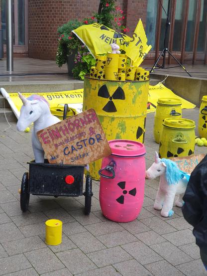 Vor dem Ahauser Rathaus: Symbolische gelbe Atommüllfässer mit Strahlenwarnzeichen. Außerdem Einhörner (Kuscheltiere) und ein Schild mit dem Text: "Einhörner existieren & der Castor ist sicher".
