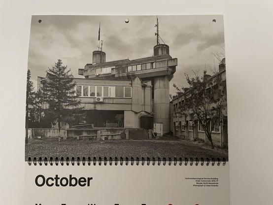 Photo of the October page of the 2025 Brutalist Calendar — illustrated with a black and white photo of the Hydrometeorological Service Building
Skopje, North Macedonia — an elevated triangular concrete building standing about a dozen meters in the air on stilt-like pylons.
