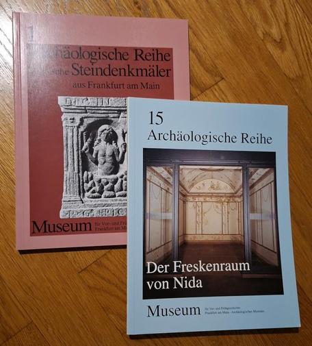 Das Foto zeigt Lesefutter: 2 Bände der Hefte "Archäologische Reihe" - Band 1, Steindenkmäler aus Frankfurt/Main und Band 15, Der Freskenraum von Nida