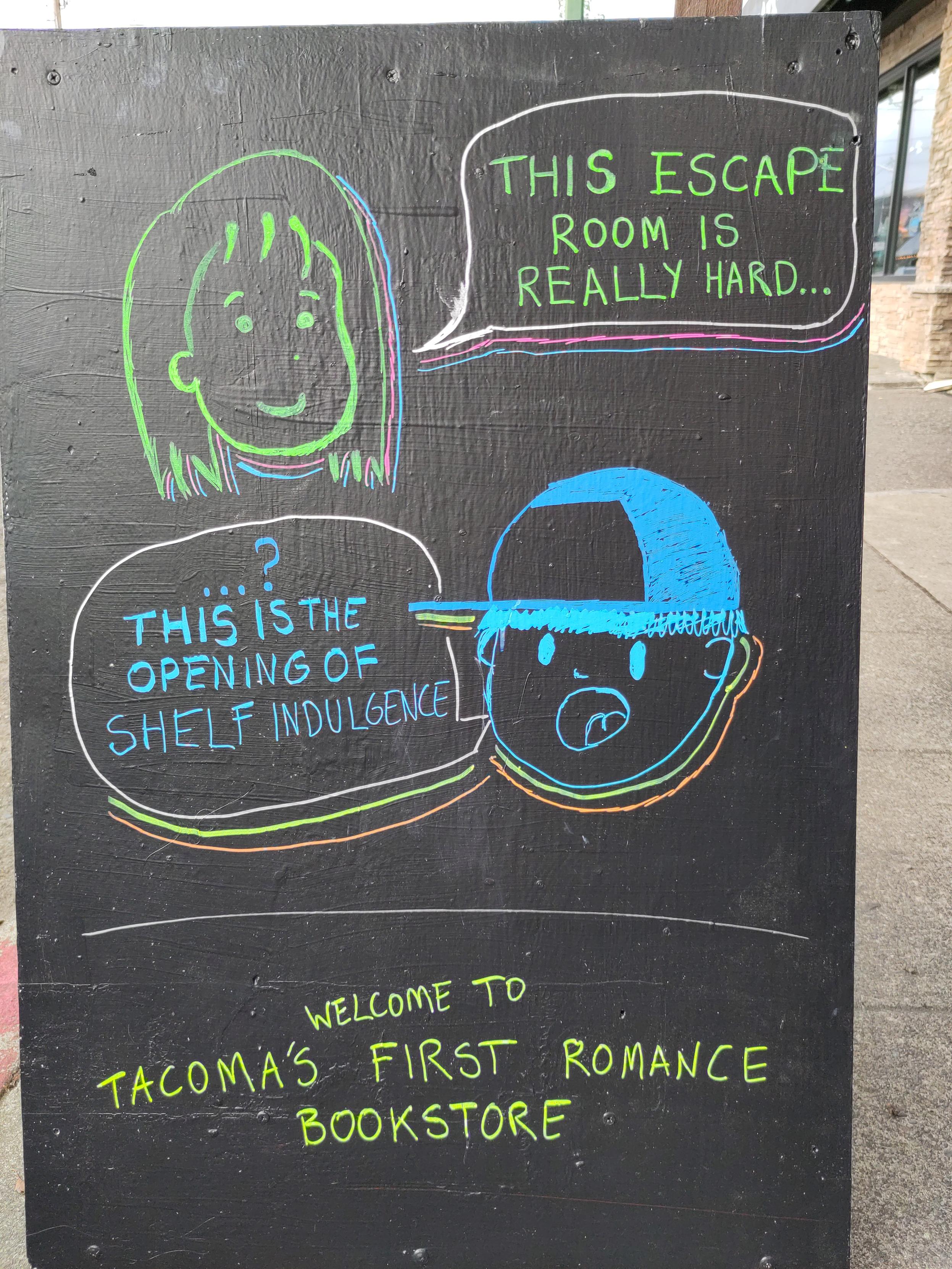 Photo of an A-frame sign on a sidewalk celebrating the opening of Shelf Indulgence in Tacoma, WA, USA. Cartoon face one says "This escape room is really hard" and cartoon face two says "...? This is the opening of Shelf Indulgence"

Beneath: "Welcome to Tacoma's First Romance Bookstore"