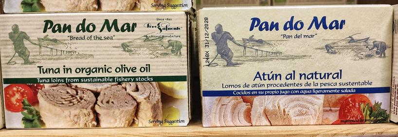 Dos latas de conserva de la marca "Pan do Mar" se muestran una al lado de la otra en una superficie de madera clara.

La lata de la izquierda, con el texto y una franja en verde, es "Pan do Mar Tuna in organic olive oil" (Atún en aceite de oliva orgánico), con la indicación "Tuna loins from sustainable fishery stocks" (Lomos de atún de pesca sostenible). La parte superior presenta una ilustración de estilo antiguo en tonos sepia, mostrando a pescadores en una playa tirando de una red y un pequeño bote. Abajo, hay una fotografía de sugerencia de presentación con varios trozos gruesos de lomo de atún, rodajas de tomate rojo fresco, hierbas verdes y una rodaja de limón.

La lata de la derecha, con detalles en azul, es "Pan do Mar Atún al natural". Su ilustración superior es similar a la anterior pero en tonos azules, mostrando también a pescadores. El texto azul indica "Lomos de atún procedentes de la pesca sustentable / Cocidos en su propio jugo con agua ligeramente salada". En la parte inferior, otra sugerencia de presentación con lomos de atún de color más claro, acompañados de tomate y hierbas verdes.