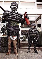 Giant riot cop puppet made of cardboard papier-mâché. Standing with much smaller real riot cops in front of the Seattle Jail on the one year anniversary of the big WTO protests in 2000.