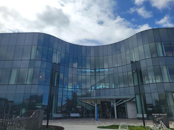 Exterior daytime photo of South San Francisco Library main branch. It's a three story modern building with a curved glass exterior.