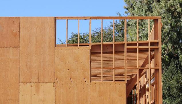 Exterior wood frame wall partially covered with plywood, with pitched shed roof rafters behind the wall (rake view).
