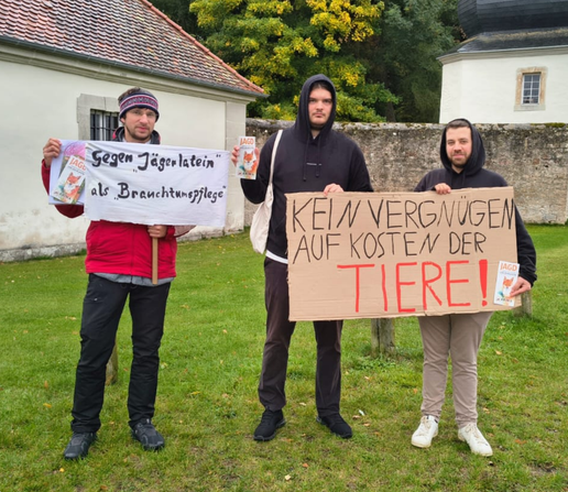 Drei Aktivisti am Schloss Fasanerie in Eichenzell während der Schleppjagd Am Welttierschutztag. Sie halten zwei Banner hoch auf denen "Gegen Jägerlatein als Brauchtumspflege" und "Kein Vergnügen auf Kosten der Tiere!" steht.