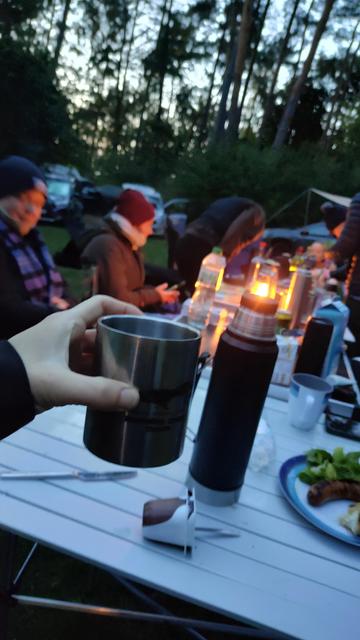 Eine Gruppe Menschen sitzt bei Kerzenschein draußen an einer Tafel  aus Campingtischen.