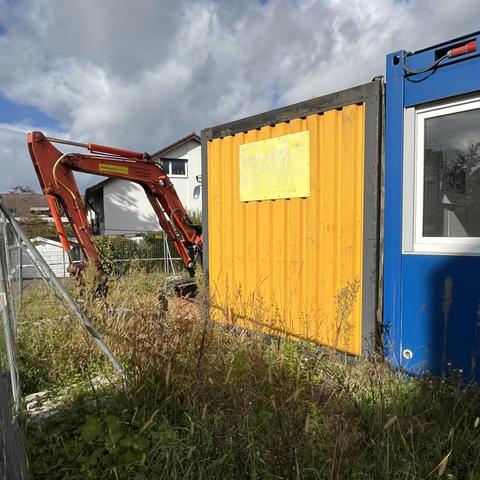 Gelbe und blaue Baustellencontainer und ein roter Bagger