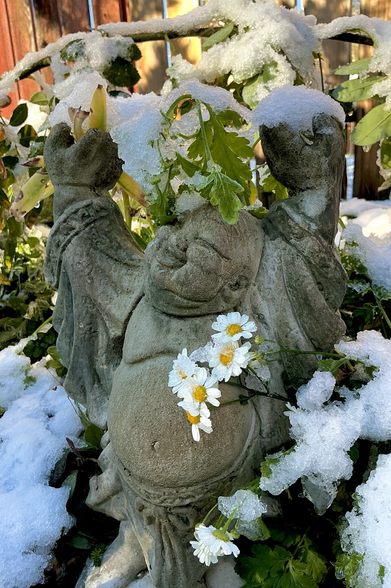 a Buddha sculpture with feverfew blooms encased in ice and snow. winter is coming.