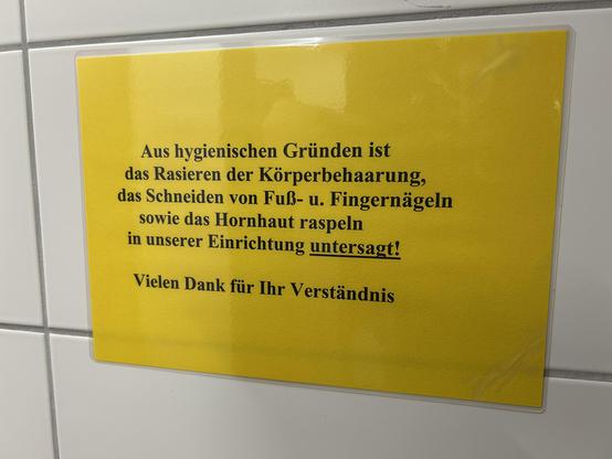 Warnschild auf gelbem Hintergrund, das das Rasieren, Schneiden und Raspeln in der Einrichtung aus hygienischen Gründen verbietet.