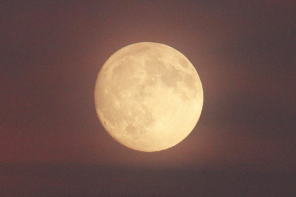 Photo of a large nearly full moon surrounded by pink clouds.