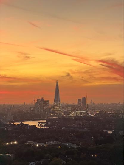 A photo of an orange and pink sunset over London. Taken from canary Wharf in the east, we face west, looking towards The Shard and Tower Bridge. 