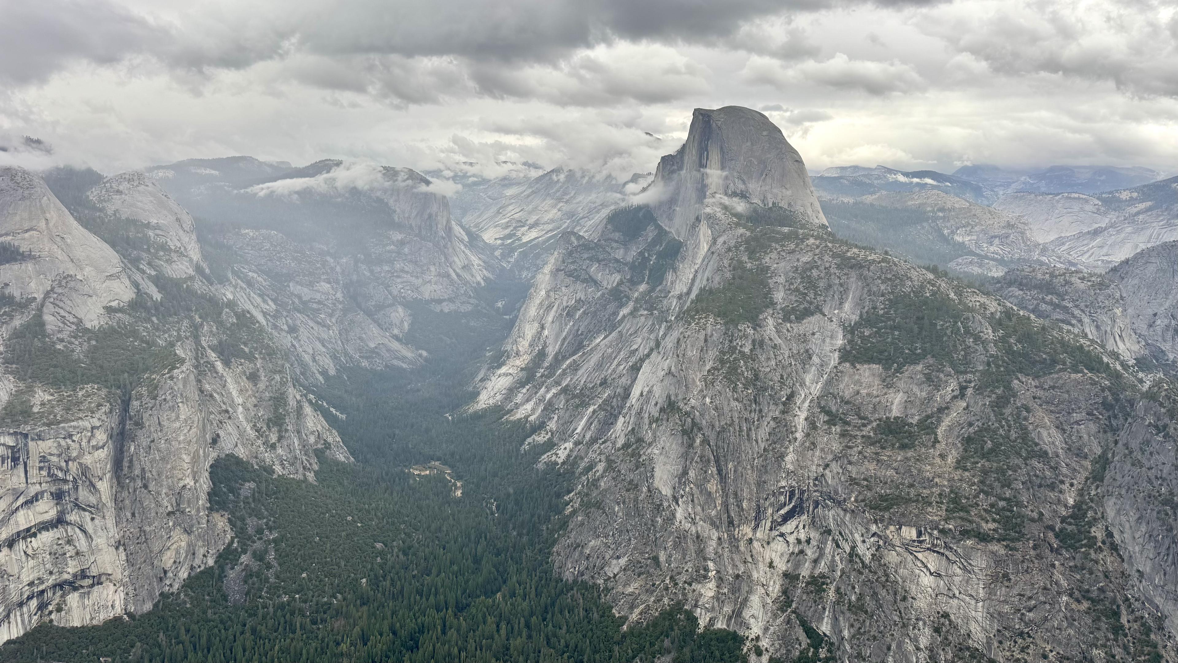 Dramatic view from on high looking up Tenaya canyon with half dome to the right side and the tree filled Yosemite valley below the grey granite cliffs.