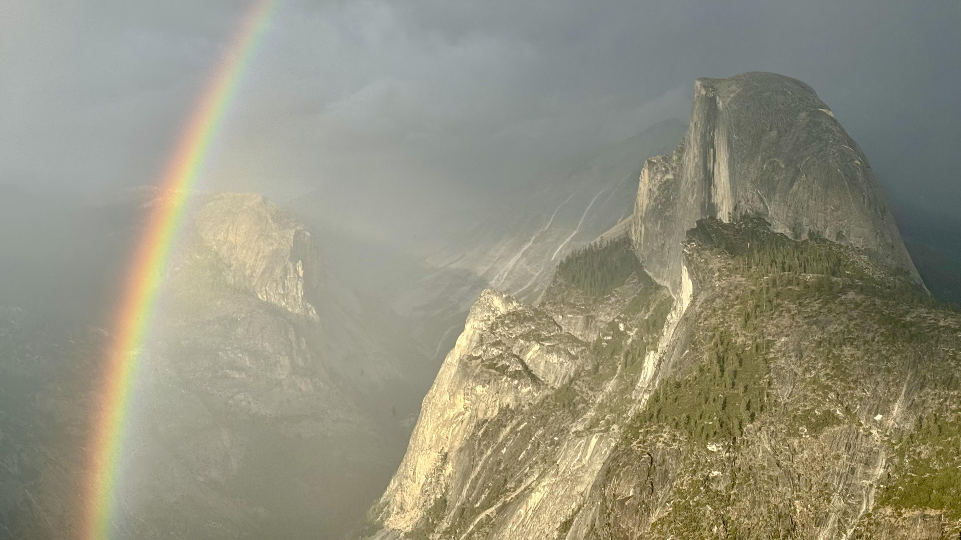 Half dome in a clearing afternoon storm, lit near sunset up the valley and encircled by a rainbow