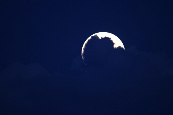 Photograph of a full moon in a dark purple sky with a cloud top mostly blocking the lower 90% of the moon.