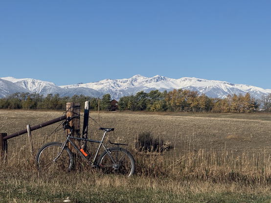 A rock hopper mountain bike leaning against a gatepost. The high peaks of the Beartooth Mountains are covered with the first snow of October in the background under bright blue skies 